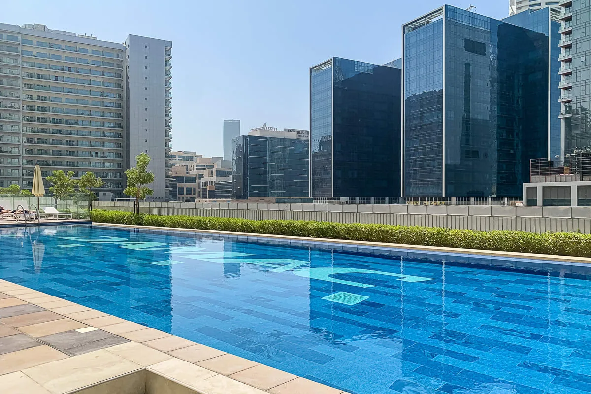 An outdoor swimming pool sits beside modern high-rise buildings.