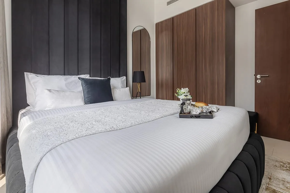 A bedroom with a neatly made bed and dark upholstered headboard.