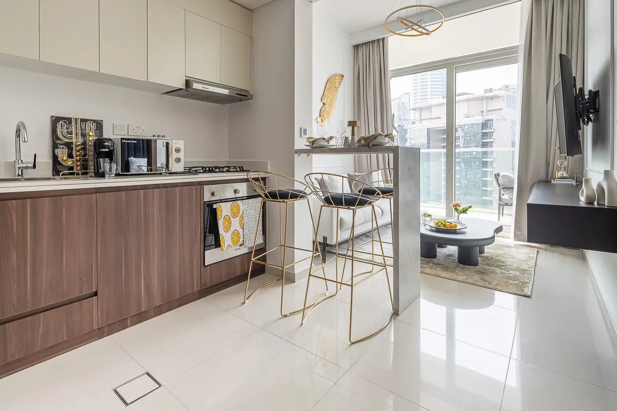 A modern kitchen opens into a bright living area with large windows.
