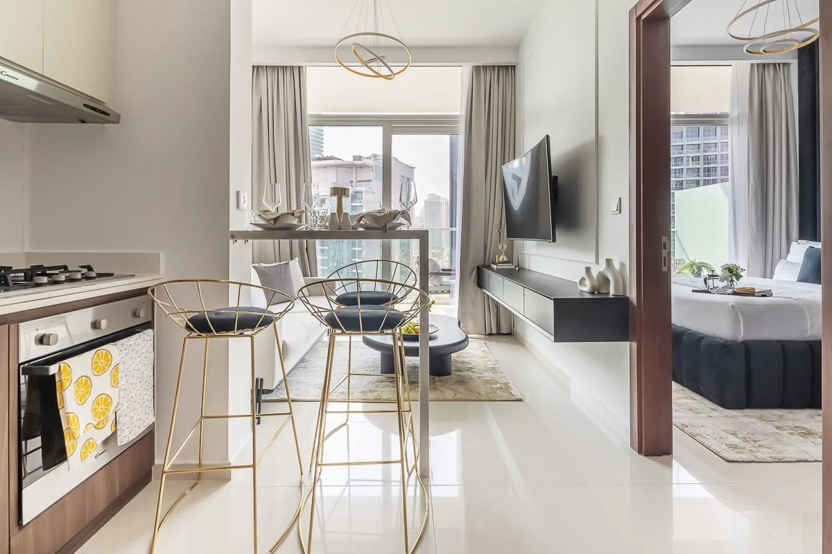 A bright open-plan living and dining area with a kitchen, large windows, and a television.