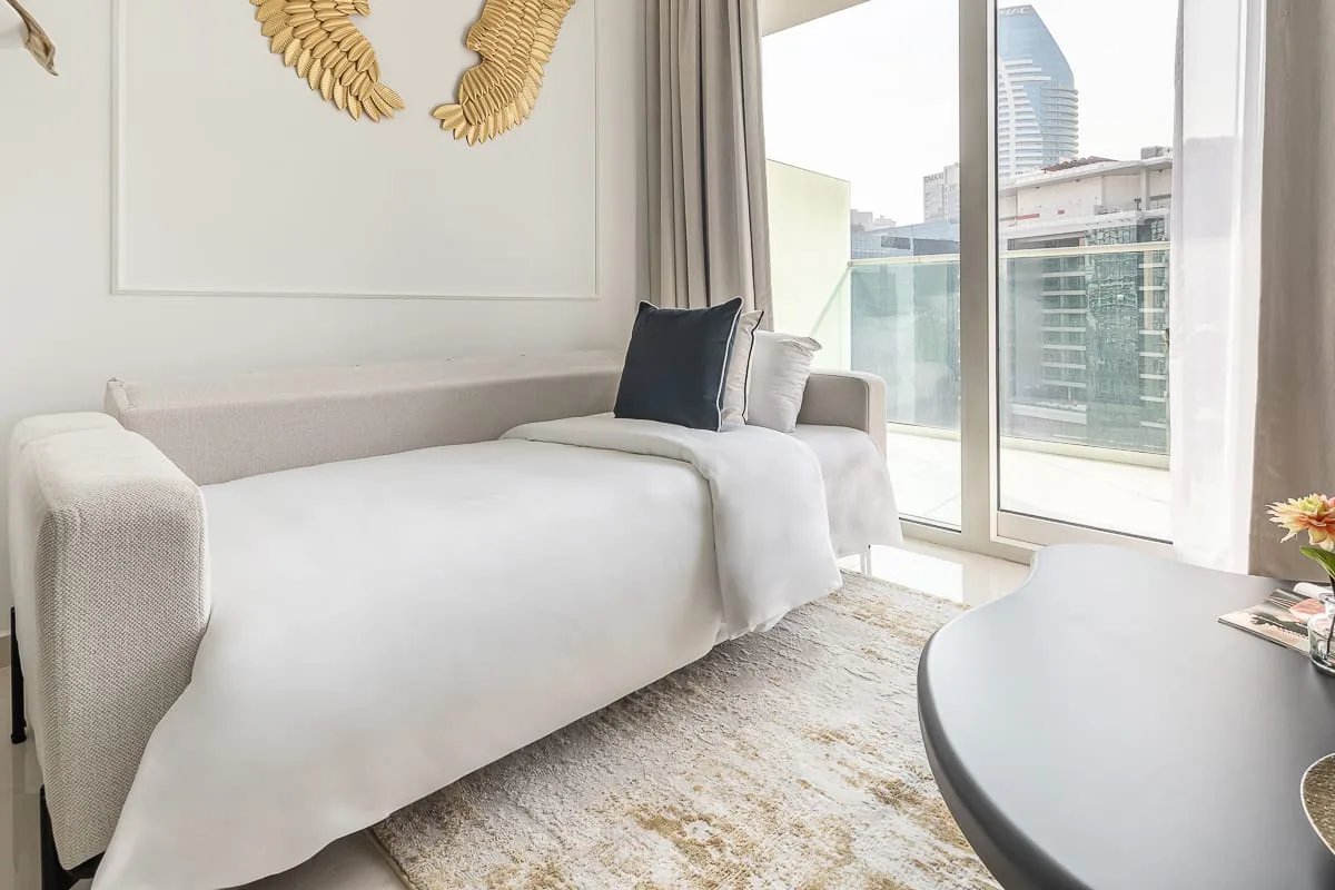 A bright bedroom with a neatly made bed beside large windows.