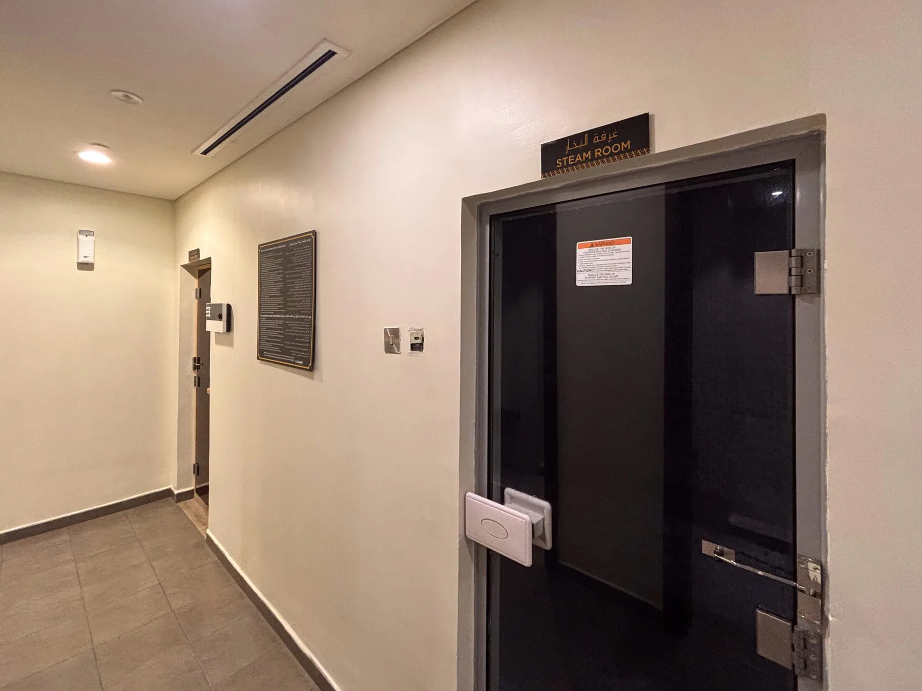 A hallway with a dark door and a steam room sign above it.