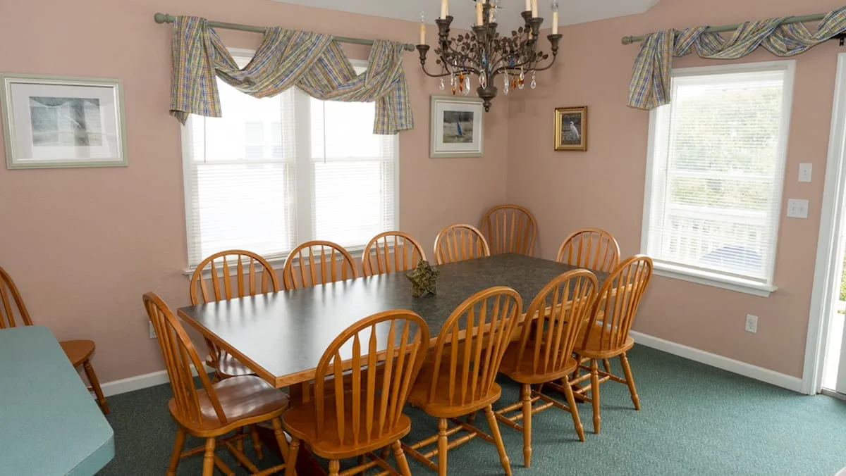 A dining room with a large table and wooden chairs beneath a chandelier.