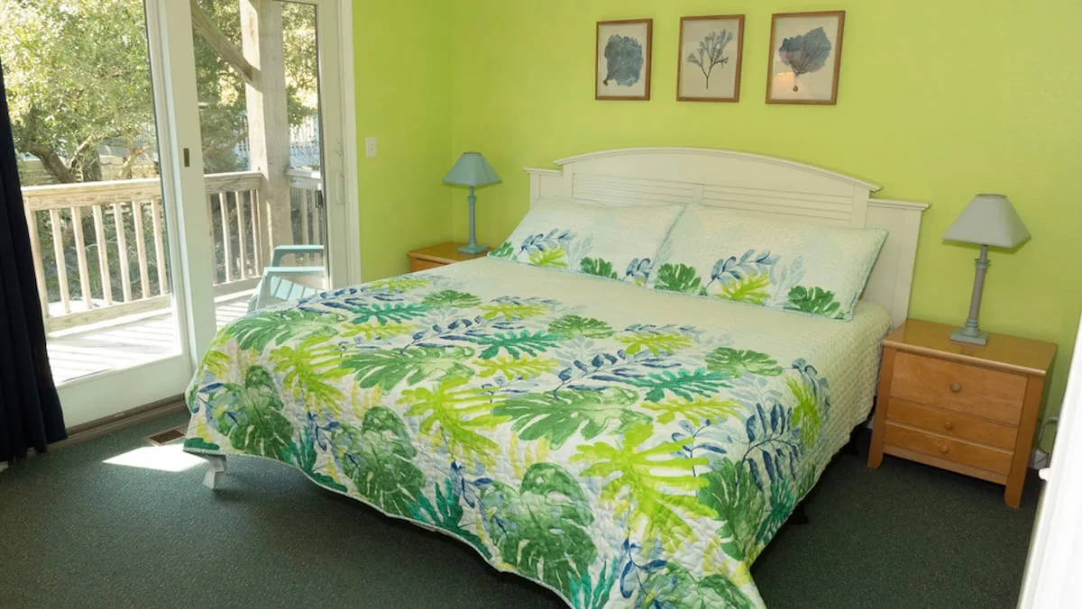A bedroom with a bed covered in a green and blue floral bedspread.