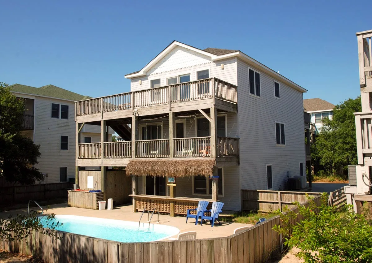 A multi-level coastal house overlooks a swimming pool and fenced patio.
