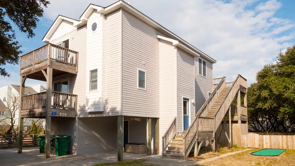 A raised coastal-style house with exterior staircases and wooden balconies.