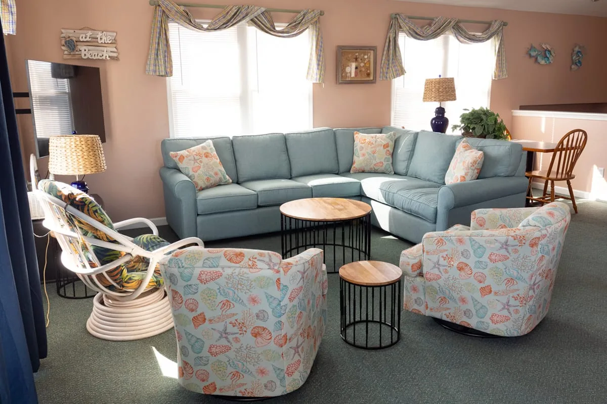 A living room with a sectional sofa, patterned armchairs, and round tables.