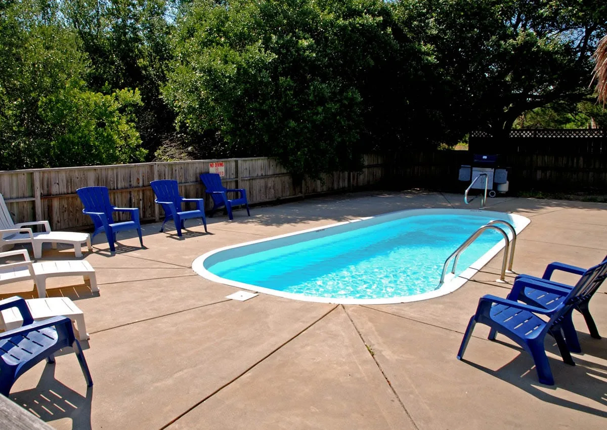 An outdoor swimming pool sits on a paved patio surrounded by trees.