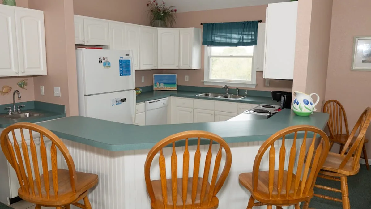 A kitchen with a curved counter, wooden seating, and white cabinets.
