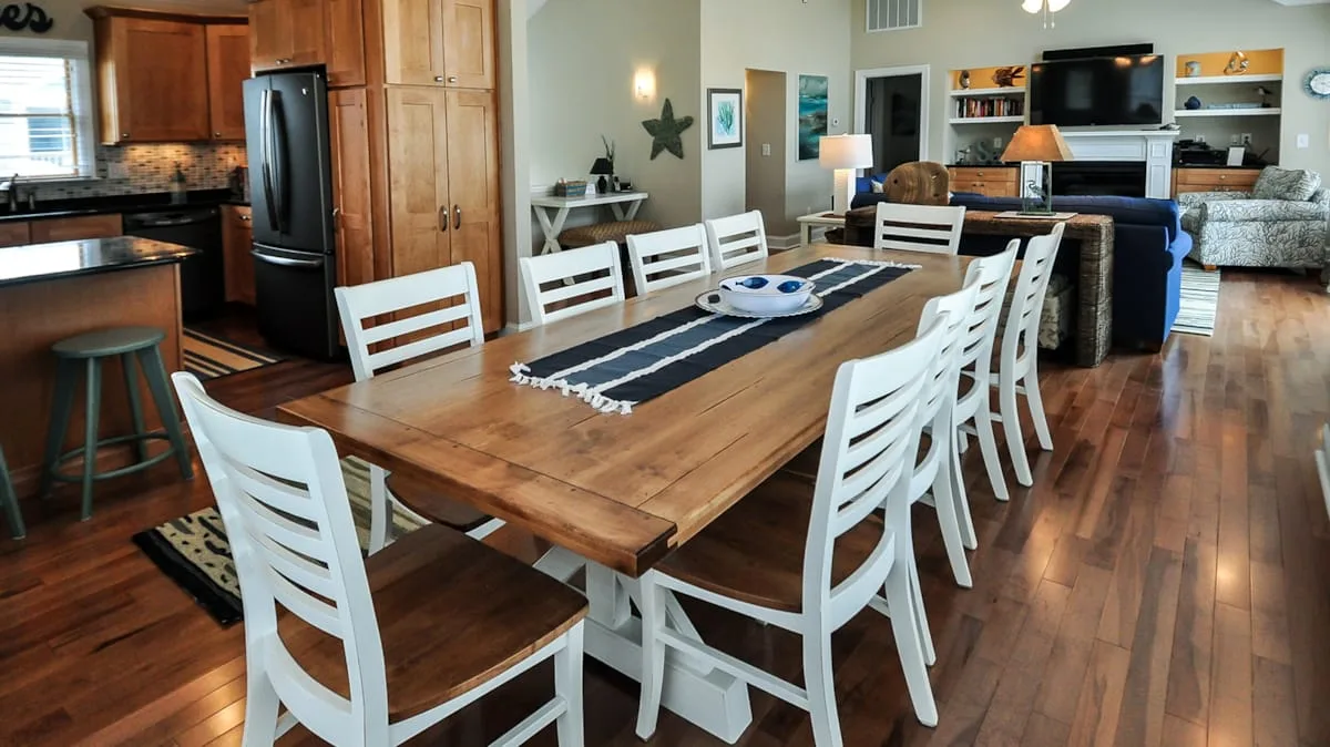 An open-plan dining and living area with a long wooden table and white chairs.