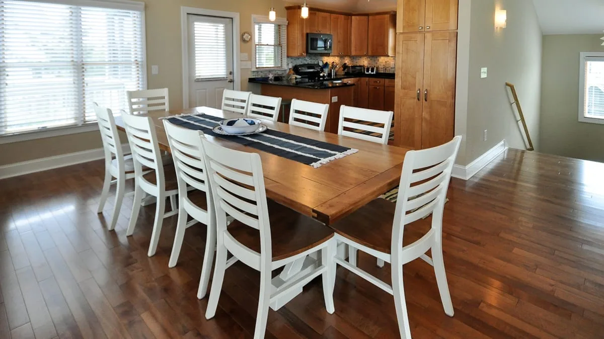 A dining area with a wooden table and white chairs beside an open kitchen.