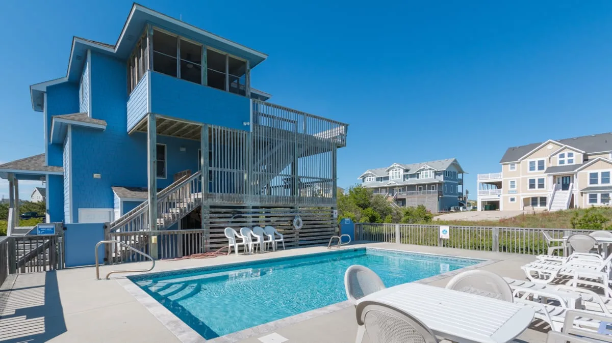 An outdoor swimming pool sits beside a blue building and white patio seating.