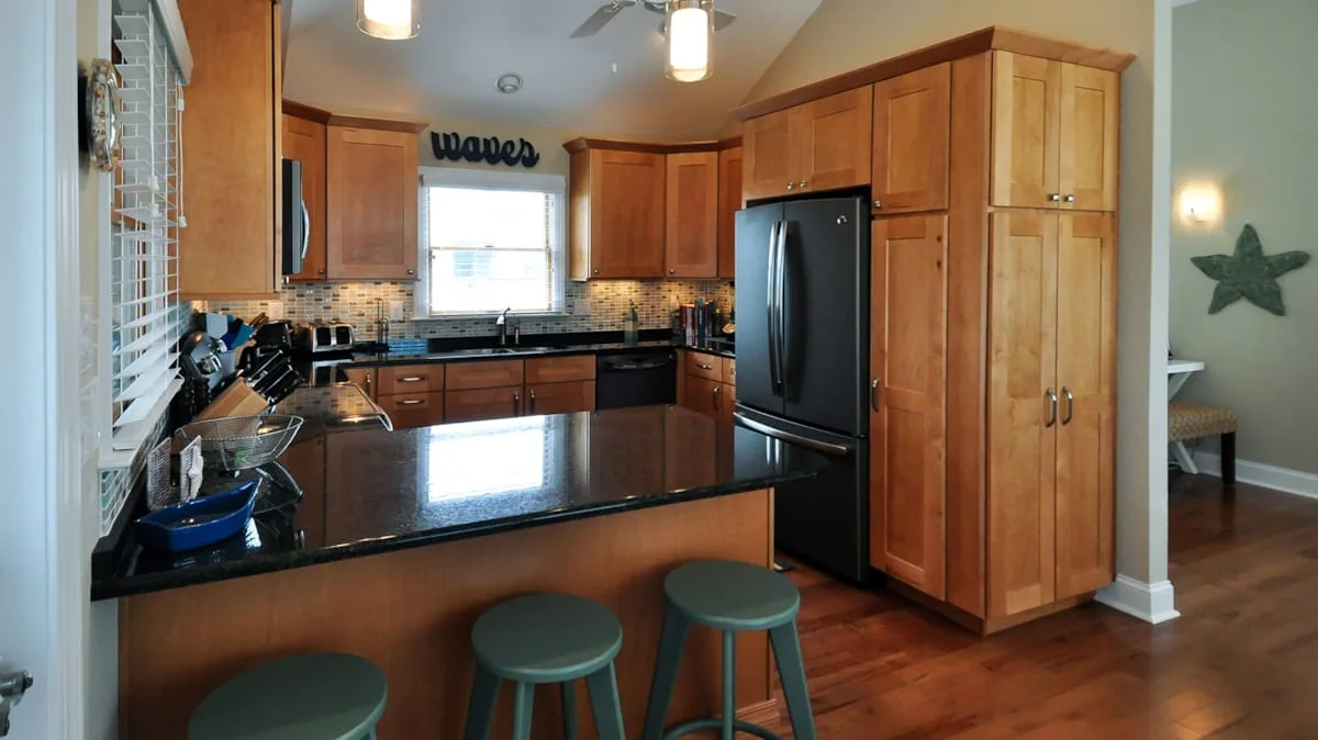 A kitchen with wooden cabinets, dark countertops, and a black refrigerator.