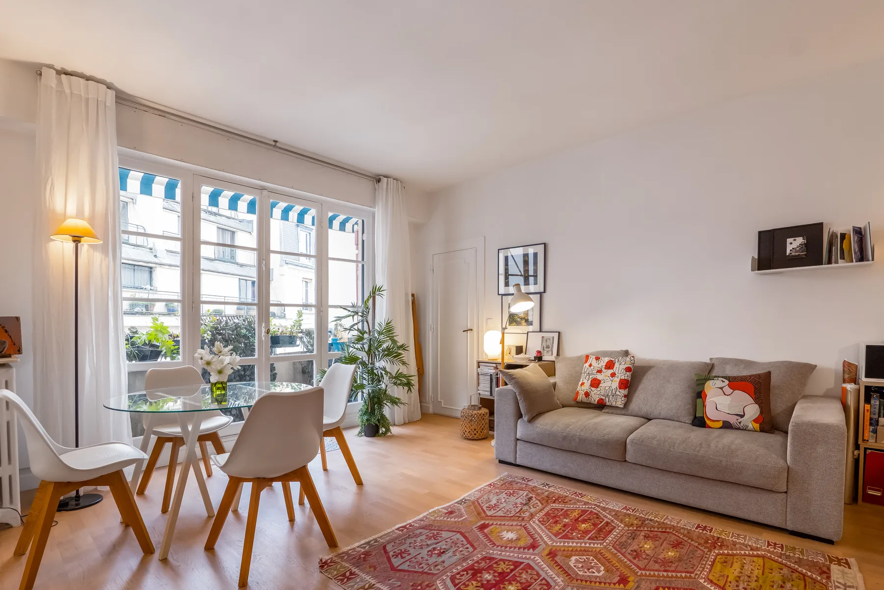 A bright living room with a gray sofa, dining table, and large windows.