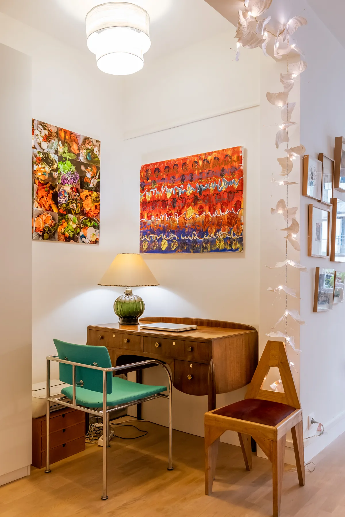 A bright room with a wooden desk, two chairs, and colorful paintings on the walls.