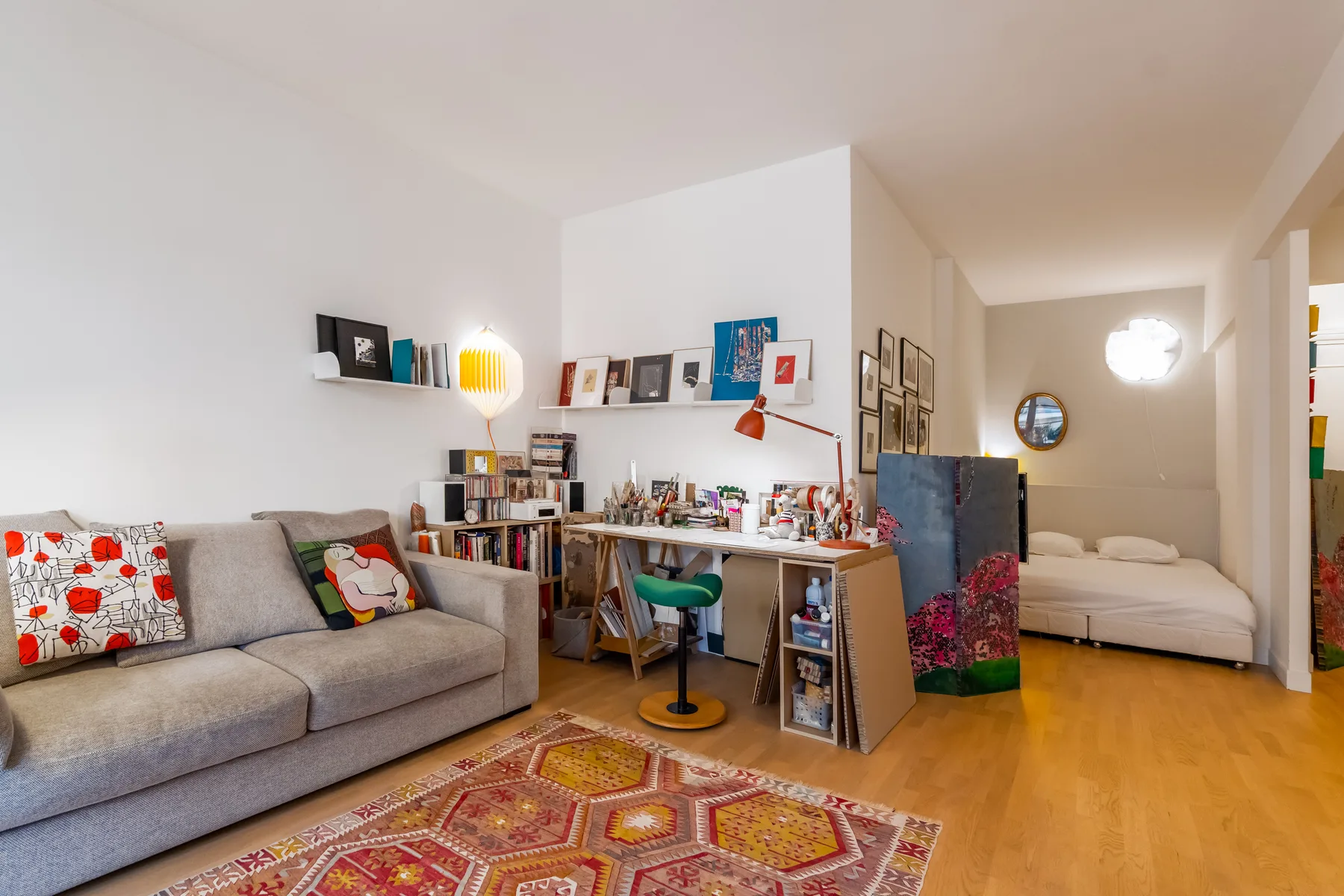A colorful living area with a sofa, work desk, and sleeping area in the background.