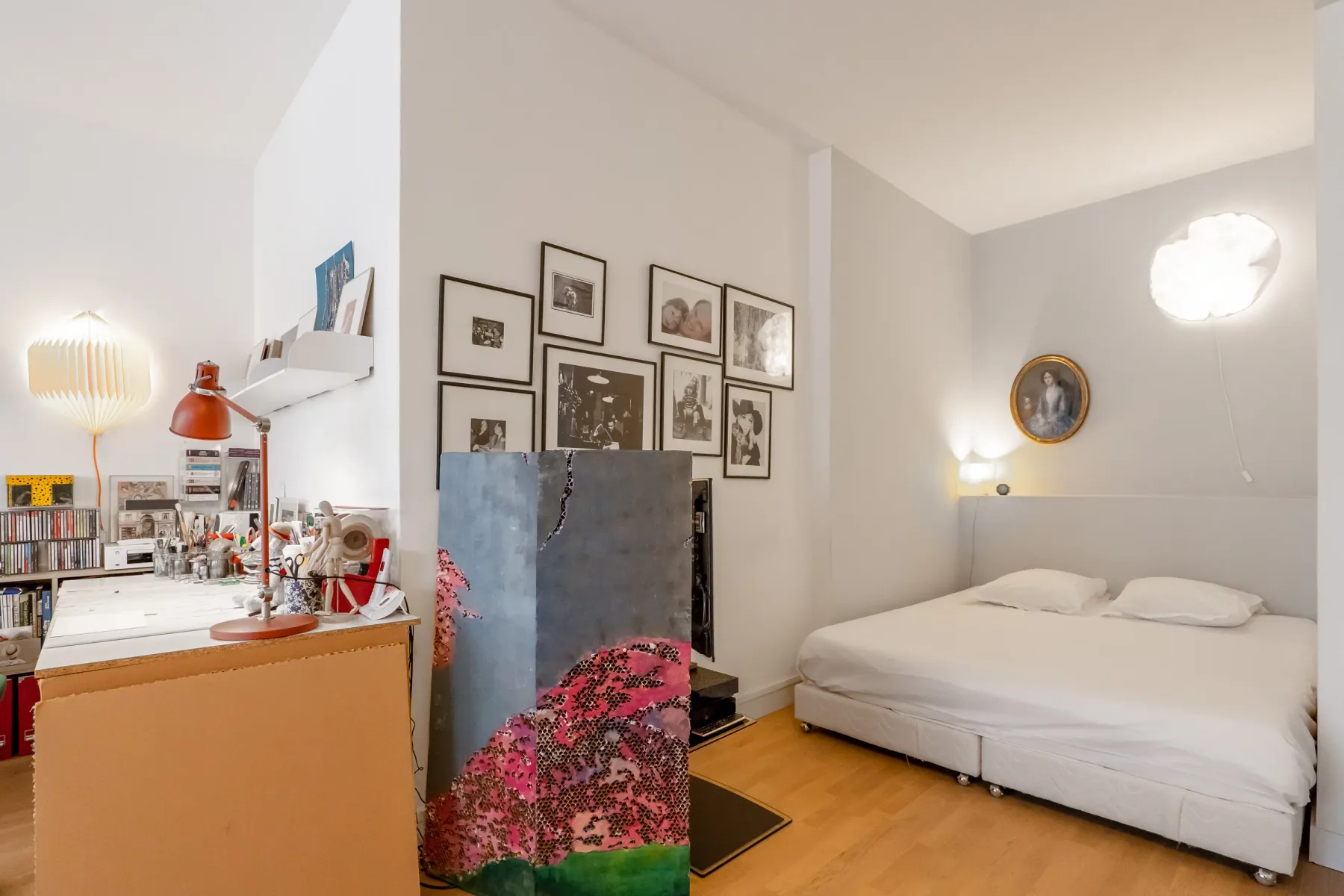 A bedroom with a bed, framed pictures, and a colorful folding screen.