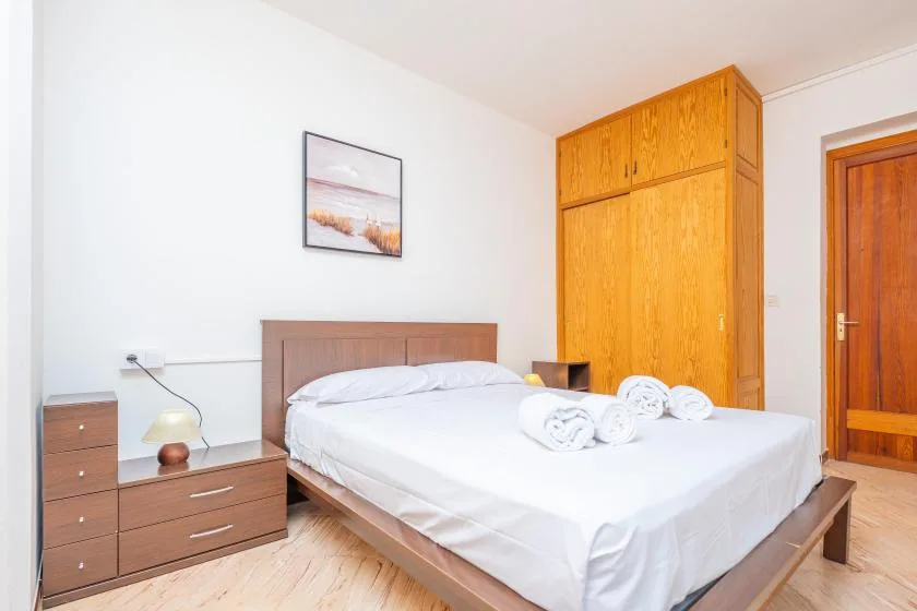 Un dormitorio con una cama bien hecha y un armario alto de madera.