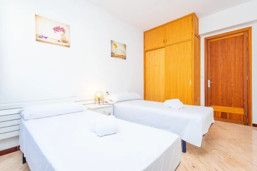Un dormitorio luminoso con dos camas, un armario de madera y una puerta de madera.