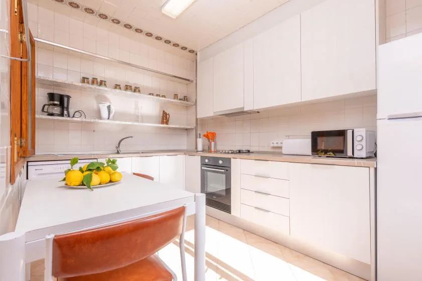Una cocina luminosa con armarios blancos, una encimera y una mesa con limones.