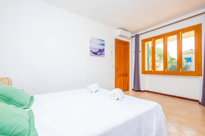 Un dormitorio con una cama blanca y una ventana grande con marco de madera.