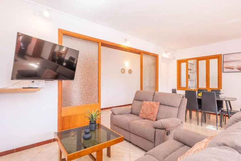 Una sala luminosa con sofá, mesa de centro de vidrio y comedor.