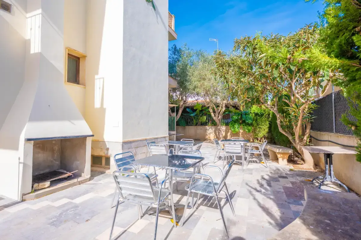Un patio soleado con asientos metálicos y una barbacoa empotrada.