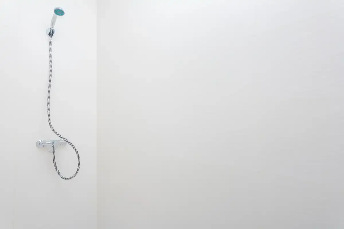 Una ducha con cabezal de mano y manguera junto a una pared lisa.