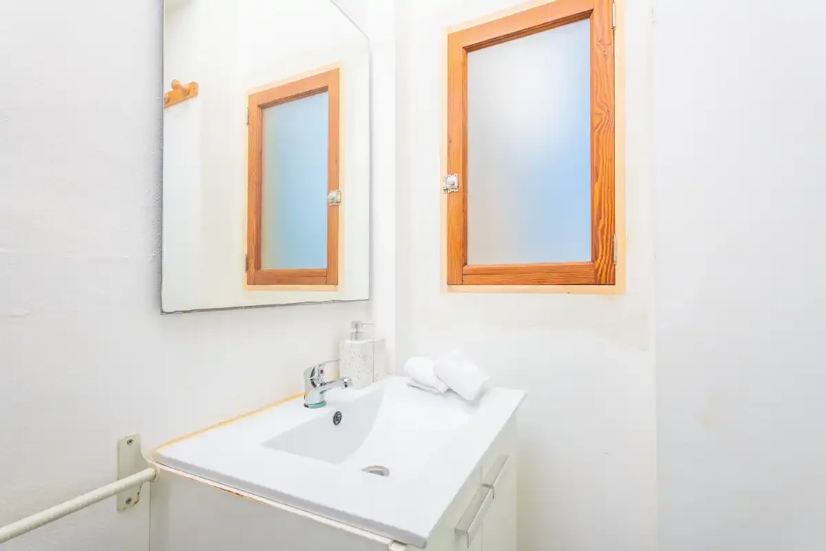 Un baño luminoso con un lavabo blanco bajo un espejo con marco de madera.