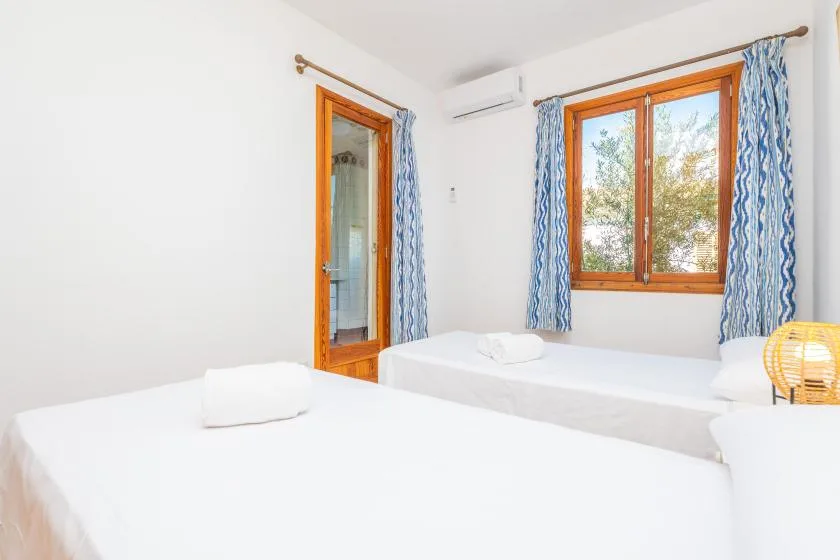Un dormitorio luminoso con ropa de cama blanca, ventanas con marcos de madera y cortinas azules.