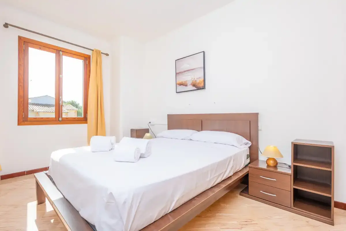 Un dormitorio luminoso con una cama tendida y una ventana.