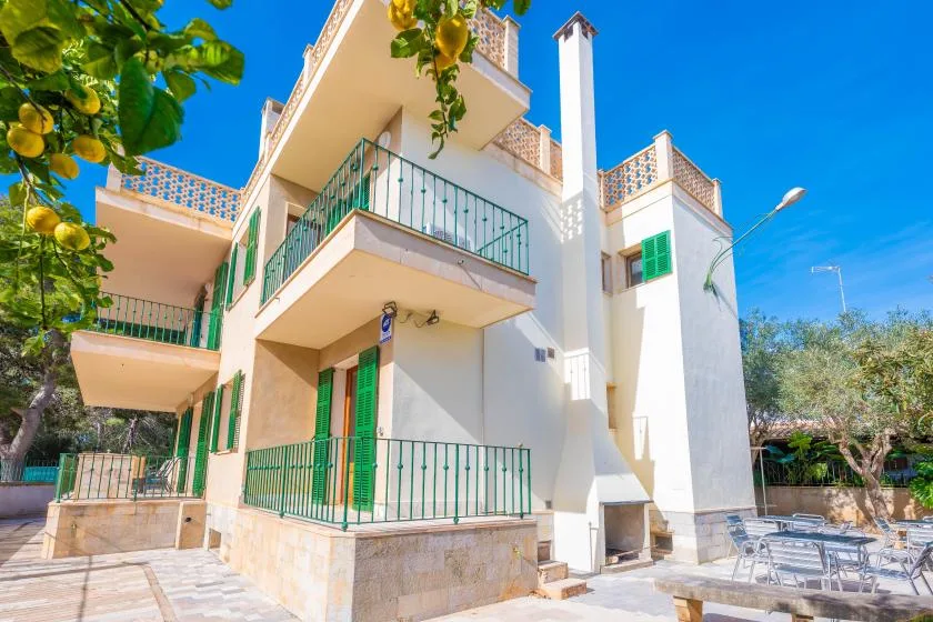 Edificio blanco de varias plantas con barandillas verdes en los balcones junto a una zona exterior pavimentada.