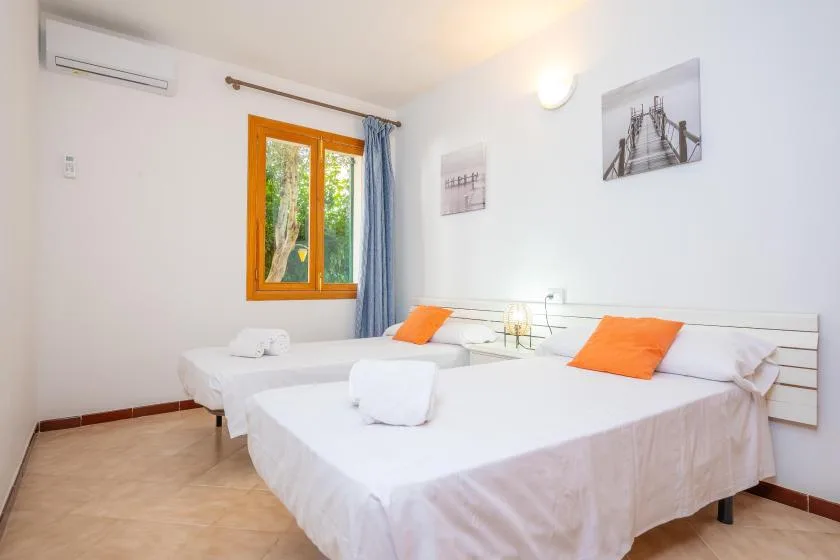 Un dormitorio luminoso con dos camas, ropa de cama blanca y cojines naranjas.