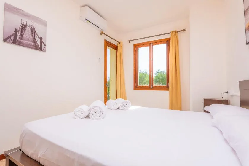 Un dormitorio con ropa de cama blanca, una ventana con marco de madera y cortinas amarillas.