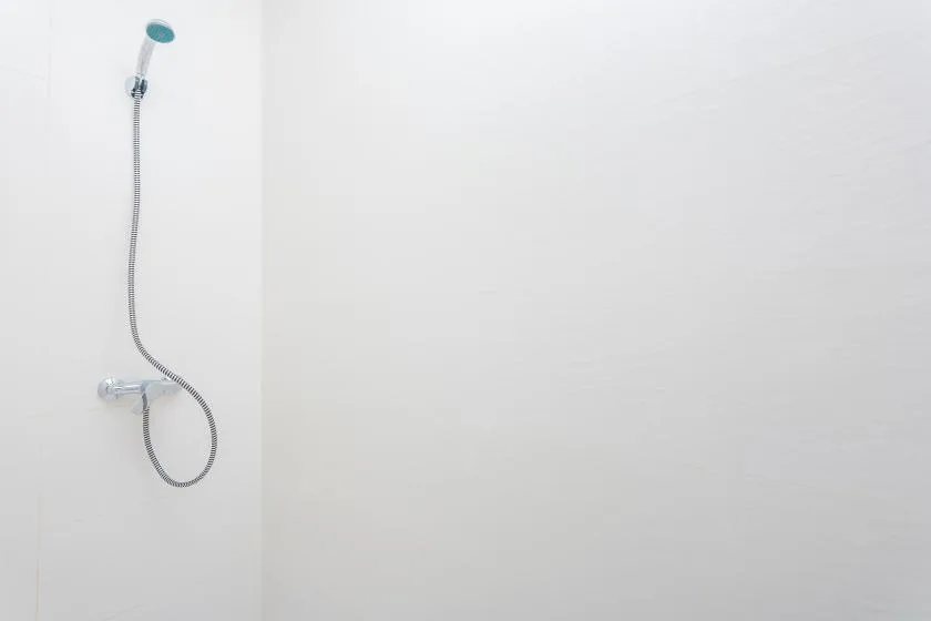 Una ducha de mano está instalada en una pared lisa de color claro.