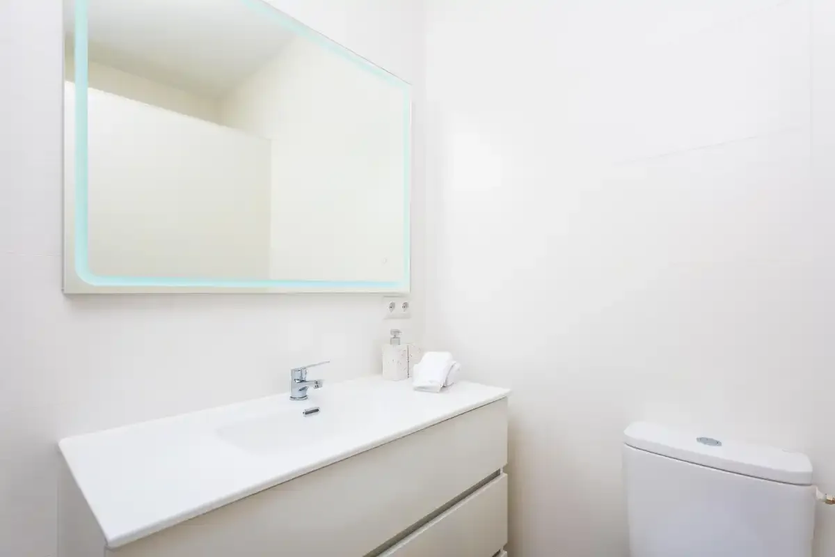 Un baño luminoso con un lavabo amplio, un espejo y un inodoro.