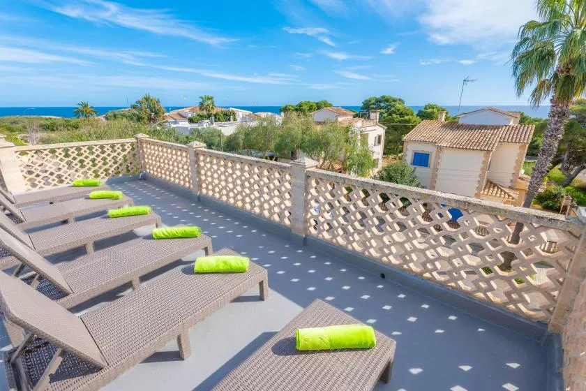 Una terraza exterior soleada con tumbonas reclinables y vistas al mar.