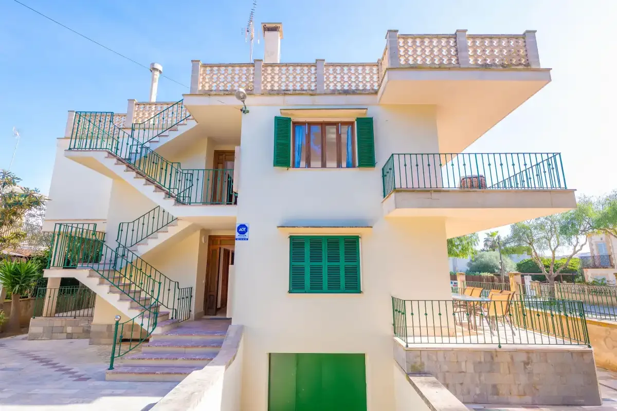 Edificio blanco de varios niveles con escaleras exteriores, balcones y contraventanas verdes.