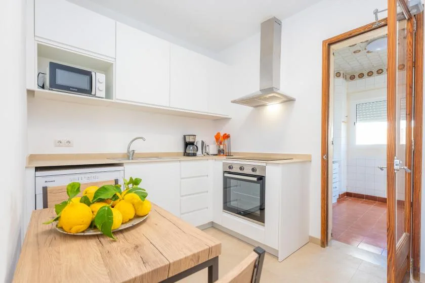 Una cocina luminosa con armarios blancos, un horno integrado y una mesa de madera.