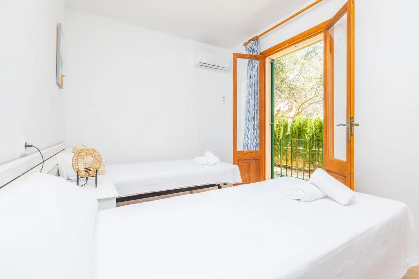 Un dormitorio luminoso con camas junto a puertas de madera abiertas que dan a un balcón.