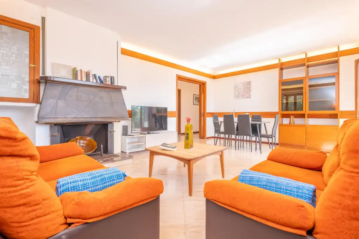 Un salón luminoso con asientos naranjas, una chimenea y un comedor.
