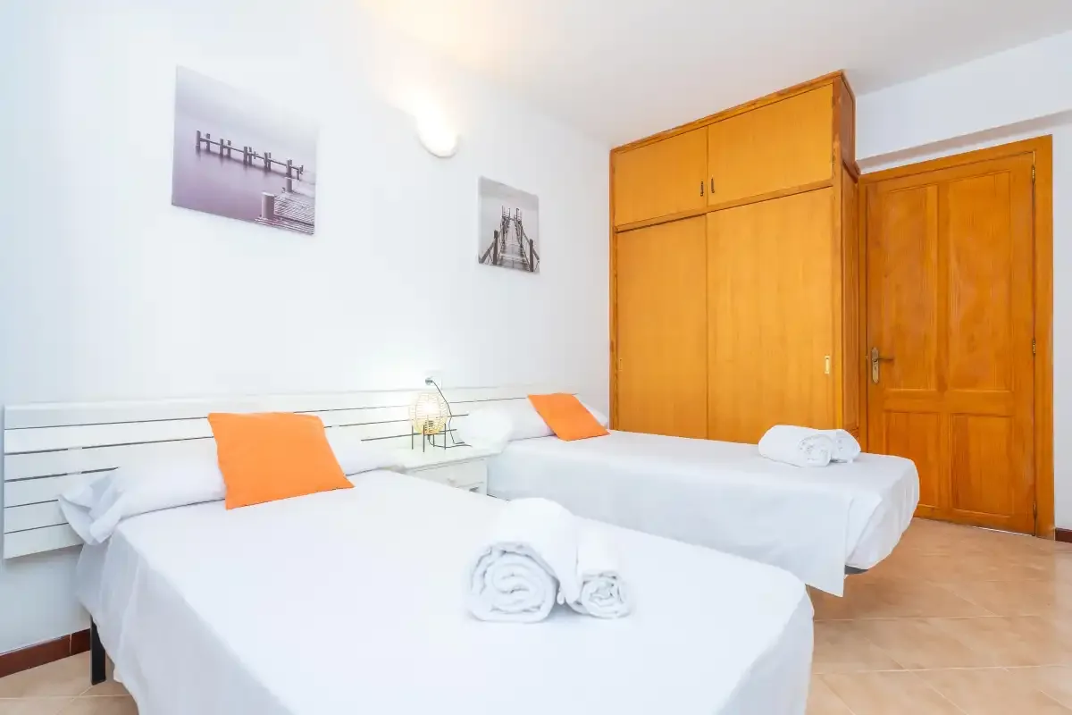 Un dormitorio luminoso con dos camas, almohadas naranjas y un armario de madera.