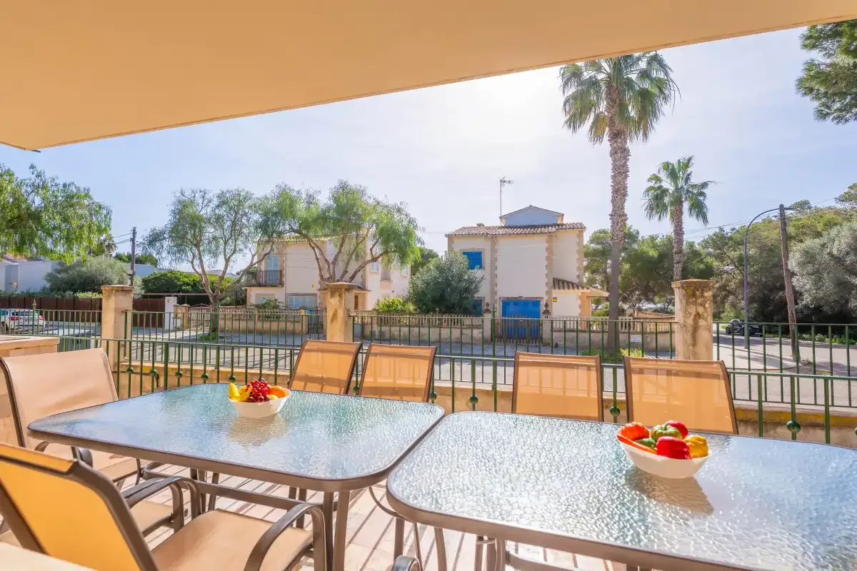 Una zona de comedor al aire libre con sombra da a una piscina cercada y edificios cercanos.