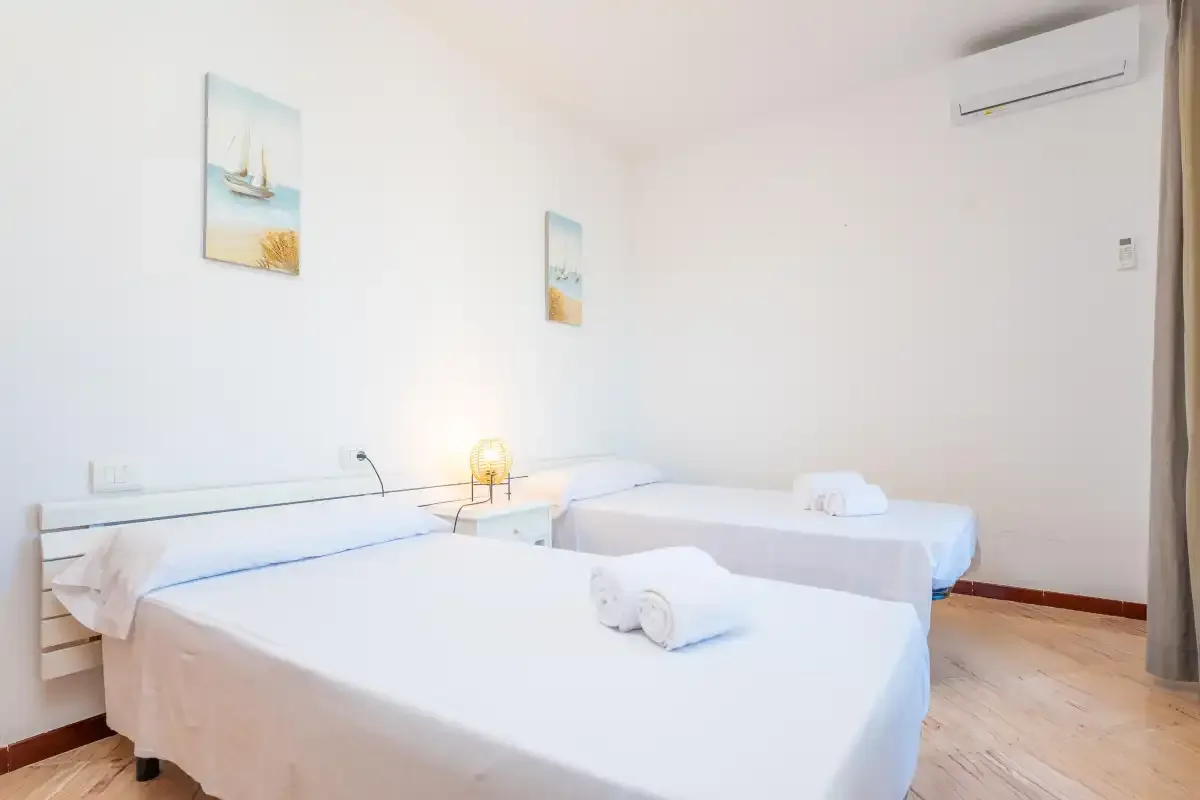 Un dormitorio luminoso con camas, cuadros en la pared y aire acondicionado.