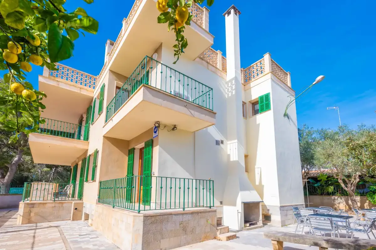 Un edificio blanco de varias plantas con barandillas verdes está junto a una zona de estar al aire libre.