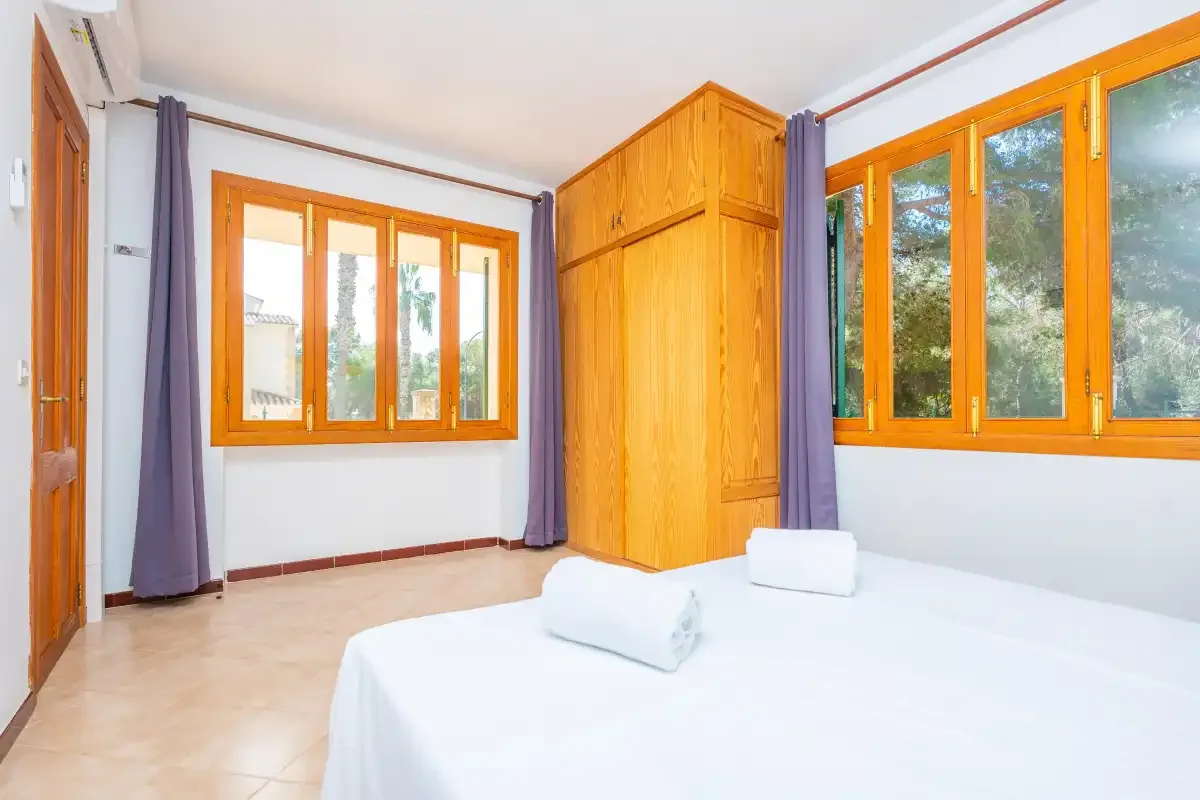 Un dormitorio con ropa de cama blanca, ventanas de madera y un armario empotrado.