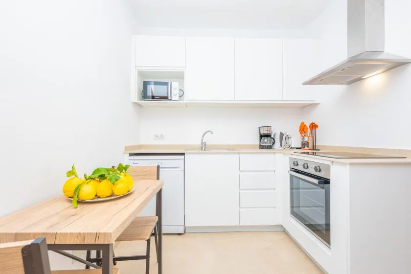 Una cocina luminosa con armarios blancos, una estufa y una mesa de comedor de madera.