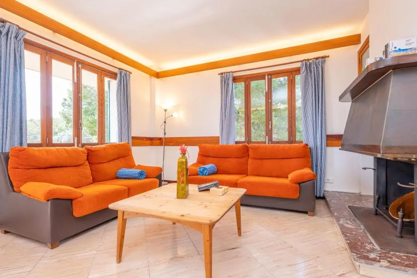 Una sala de estar con asientos naranjas, ventanas grandes y una mesa de centro de madera.