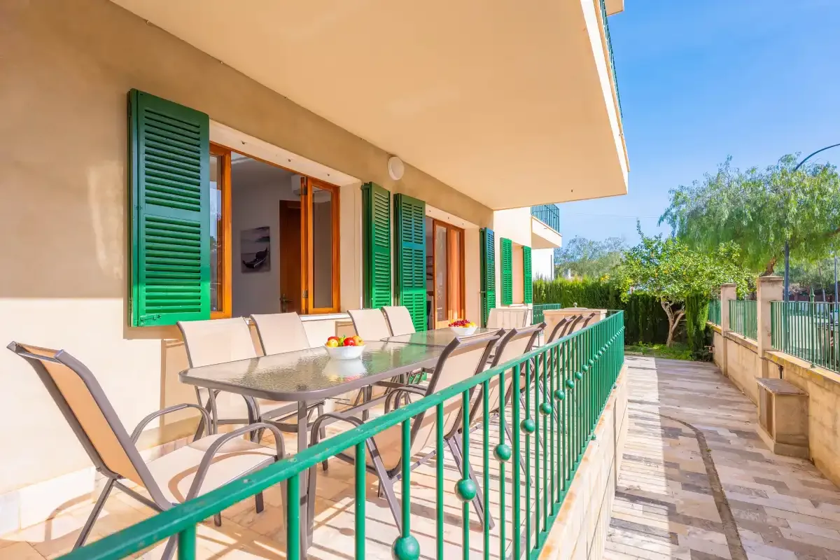 Una terraza soleada con asientos al aire libre, barandillas verdes y ventanas abiertas.