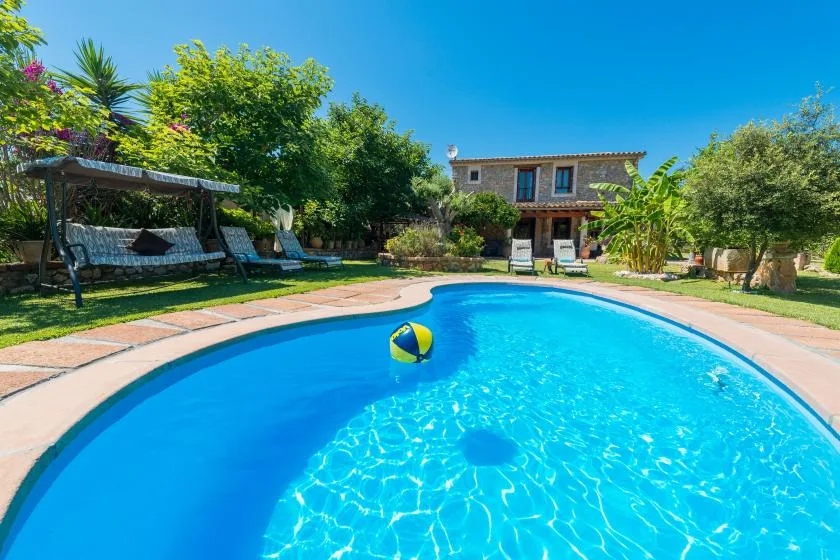 An outdoor swimming pool beside a landscaped garden and stone house.